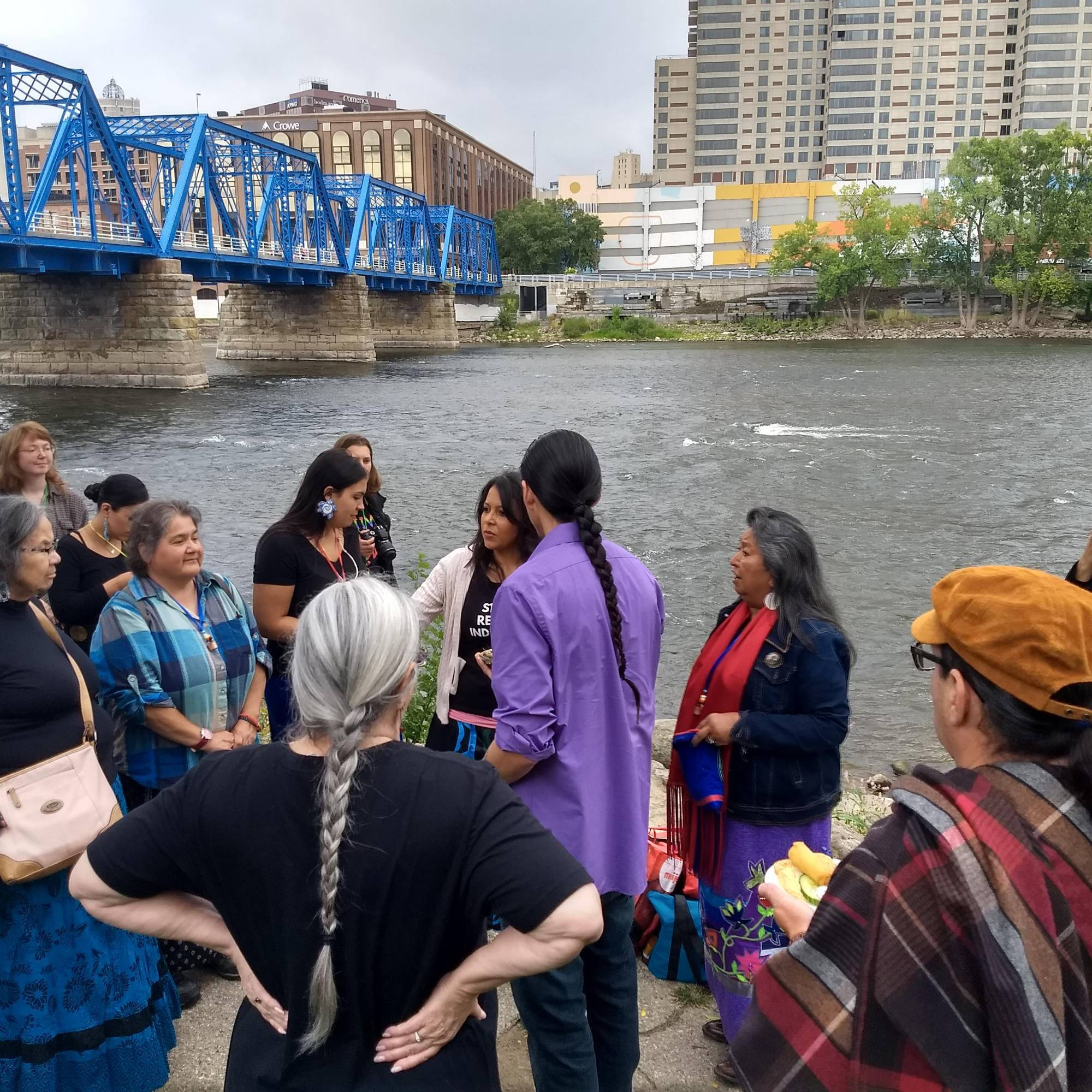 Group of individuals performing a ceremony at the river's edge downtown Grand Rapids.